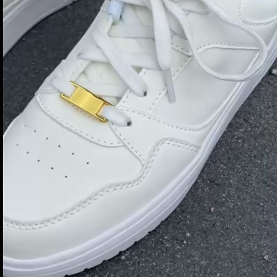 Weiße Sneaker mit goldenem Sneakeez Schuhcharm auf Asphalt – minimalistischer Schuhschmuck in edlem Look für elegante Sneaker-Styles