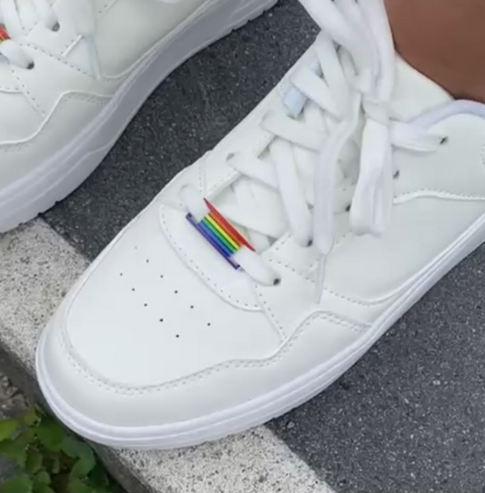 Weiße Sneaker mit Pride Sneaker Charms in Regenbogenfarben auf Asphalt – Sneakeez Schuhschmuck in Bewegung beim Gehen